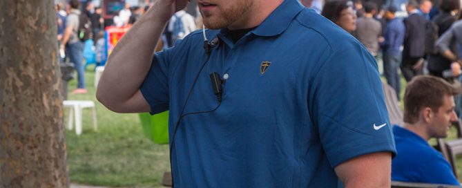 Knight armed security guard standing at an event, communicating through earpiece at outdoor venue.