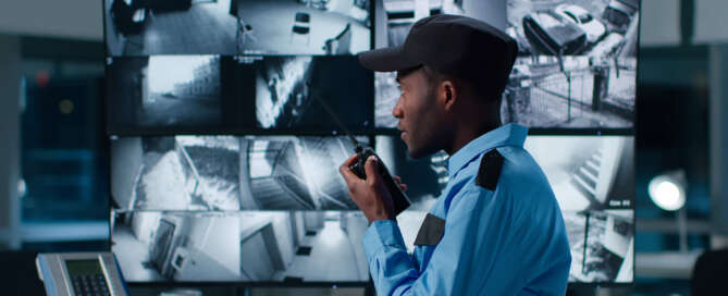 Office building security guard in front of a bank of monitors speaking into a walkie-talkie